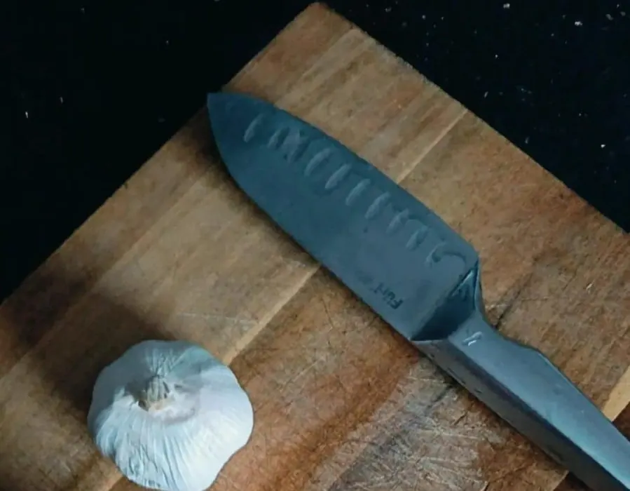 A knife and a bulb of garlic on a wooden board